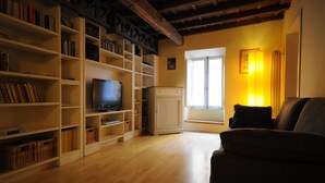 Uma sala de estar com televisão, estantes de livros, um sofá e uma janela com cortinas.