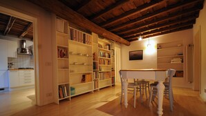 Um quarto amplo com piso de madeira, uma mesa de jantar com cadeiras e estantes embutidas repletas de livros.