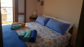 Un dormitorio con cama, almohadas, una mesita de noche, una lámpara y toallas enrolladas.