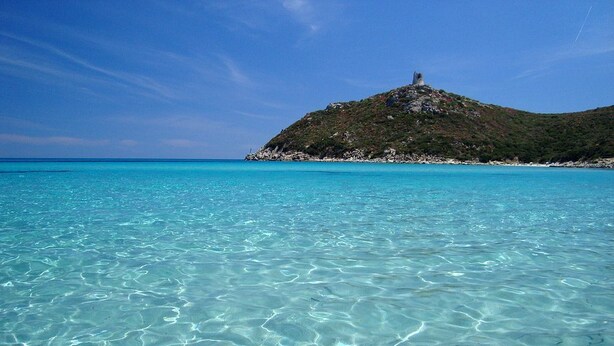Un mar turquesa y transparente con una isla rocosa al fondo.