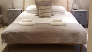 A neatly arranged bedroom with a large bed, two bedside tables, a painting above the bed, and a carpeted floor.