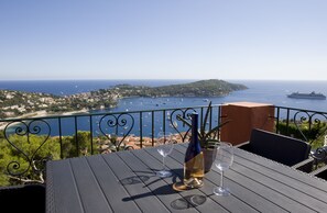 A table with a bottle of wine and two glasses, overlooking a coastal view with boats and a cruise ship. - Apartment Rooftop Villefranche-Sur-Mer (Villefranche-Sur-Mer)