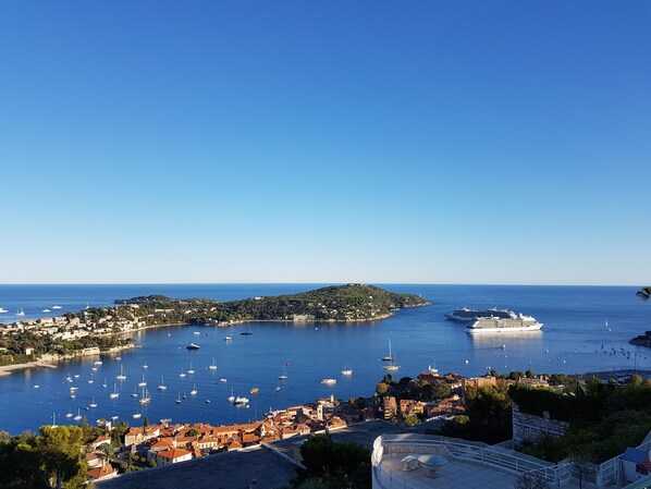 A coastal town with a marina filled with boats, a large cruise ship docked, and a prominent hill with buildings. - Apartment Rooftop Villefranche-Sur-Mer (Villefranche-Sur-Mer)