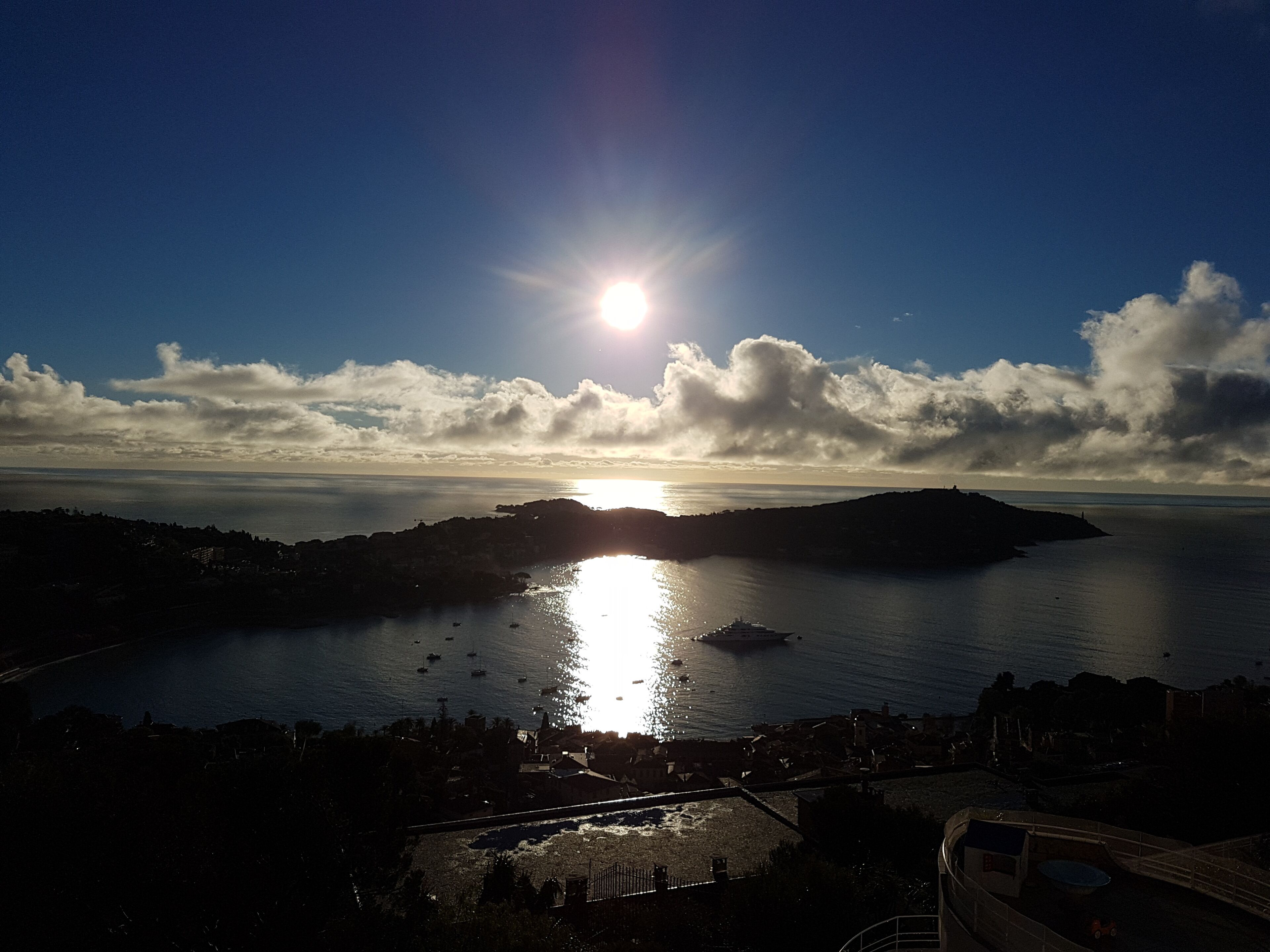 A coastal landscape with a body of water, a bridge, and a distant sun.