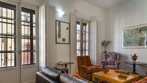 A living room with a leather sofa, a floral armchair, a wooden coffee table, and a painting on the wall. - House with terrace in the center of Seville with wifi, air conditioning and garage (Sevilla)