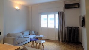 A living room with a sofa, two small tables, a radiator, and a TV mounted on the wall. - Athens Modern Apartment next to Syntagma Square  (Athina)