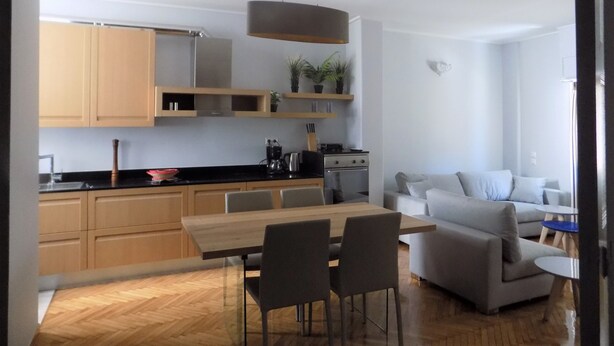 A modern kitchen with wooden cabinets, a dining area with a table and chairs, and a living room with a sofa and a coffee table. - Athens Modern Apartment next to Syntagma Square  (Athina)