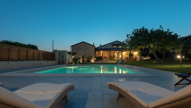 A swimming pool with lounge chairs, a wooden fence, and a house in the background. - Casa Natia - Luxury Villa with pool (Modica)