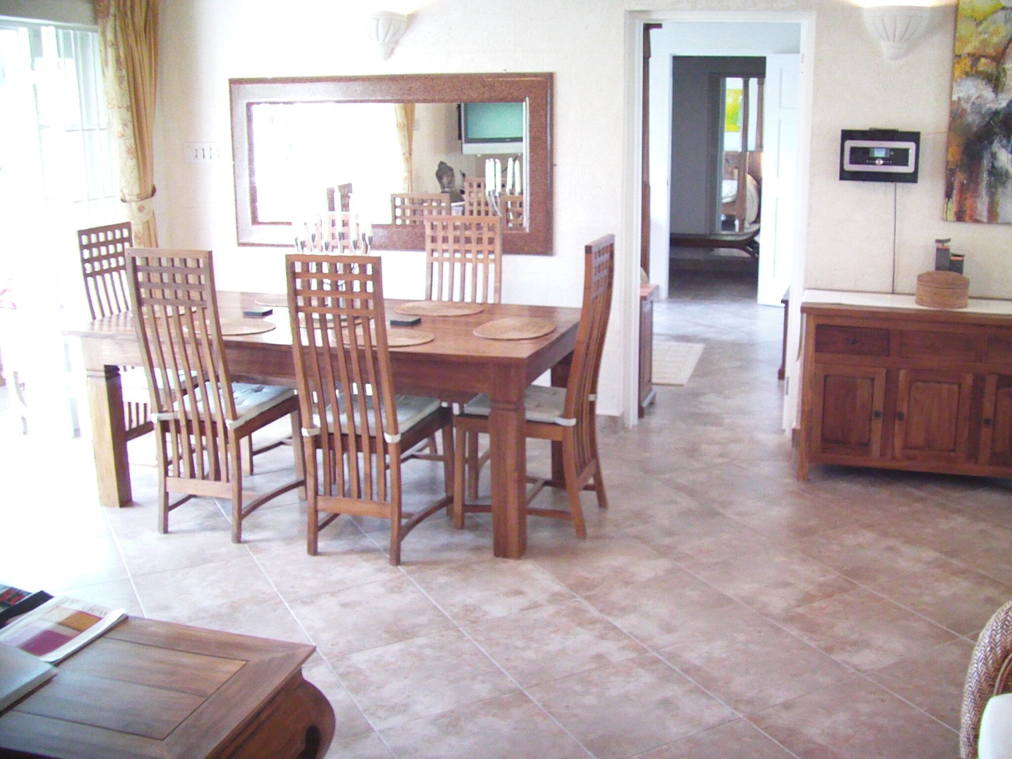 A dining area with a wooden table and chairs, a large mirror above the table, and a cabinet with a television on the wall.
