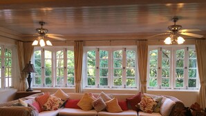 Ein gemütliches Wohnzimmer mit Korbmöbeln, einer Sofagarnitur, zwei Holznachttischen und einem Deckenventilator.