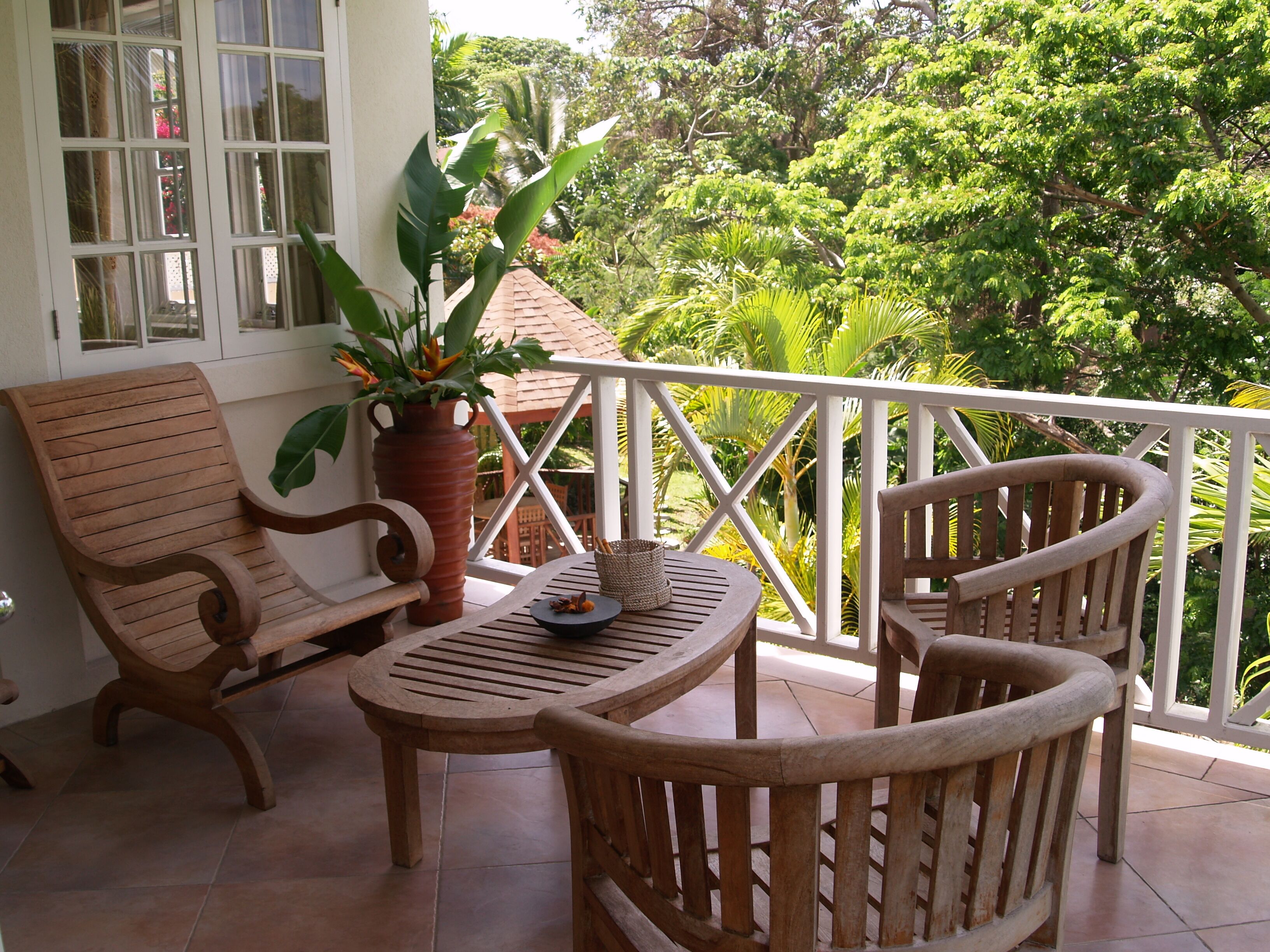 A wooden deck with two chairs and a table, surrounded by a white railing, overlooking a lush garden.