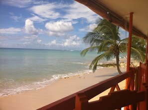 Une vue sur la plage avec une balustrade en bois, des palmiers et un ciel dégagé.