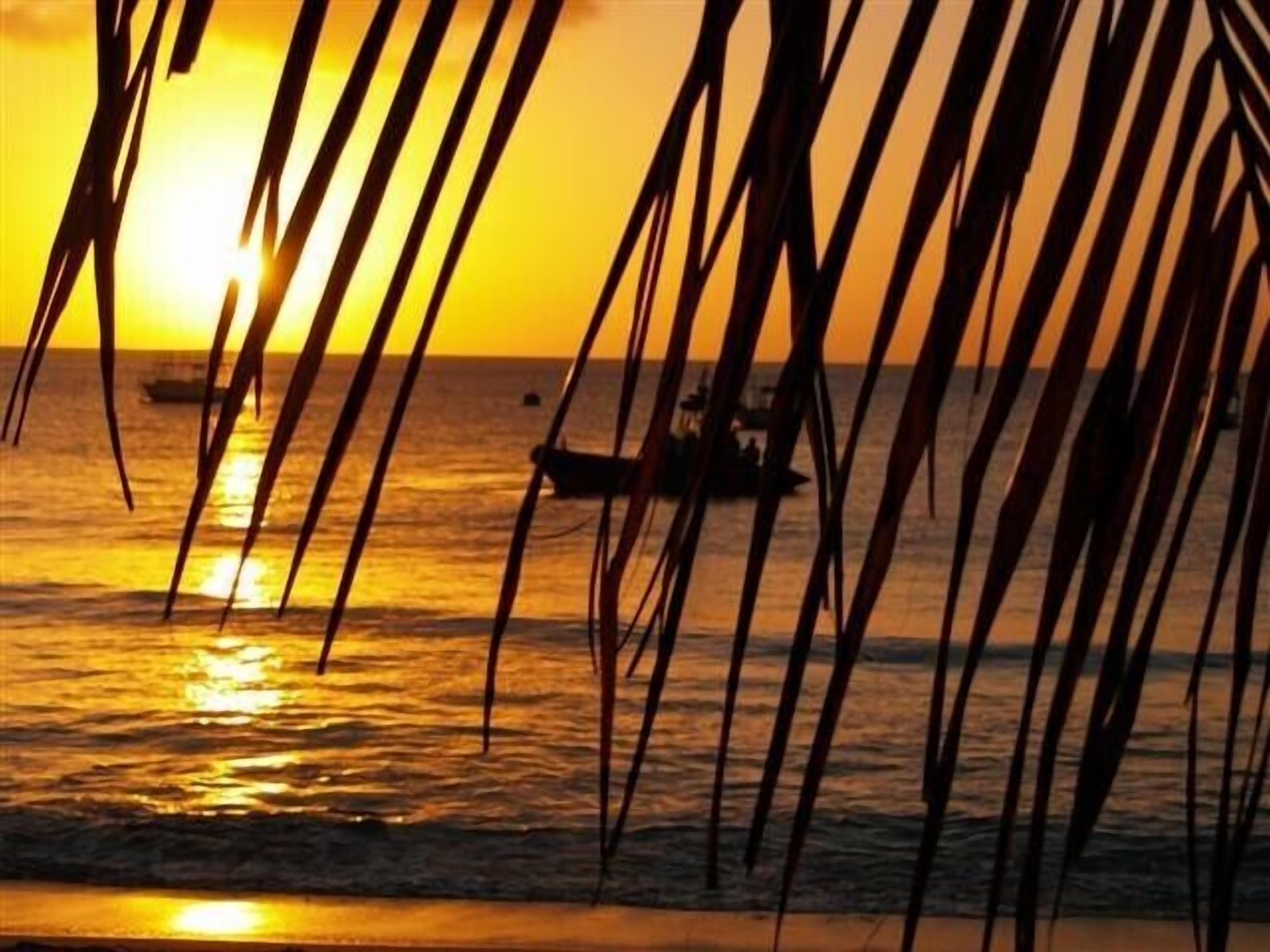 A sunset over the ocean with a boat in the distance.