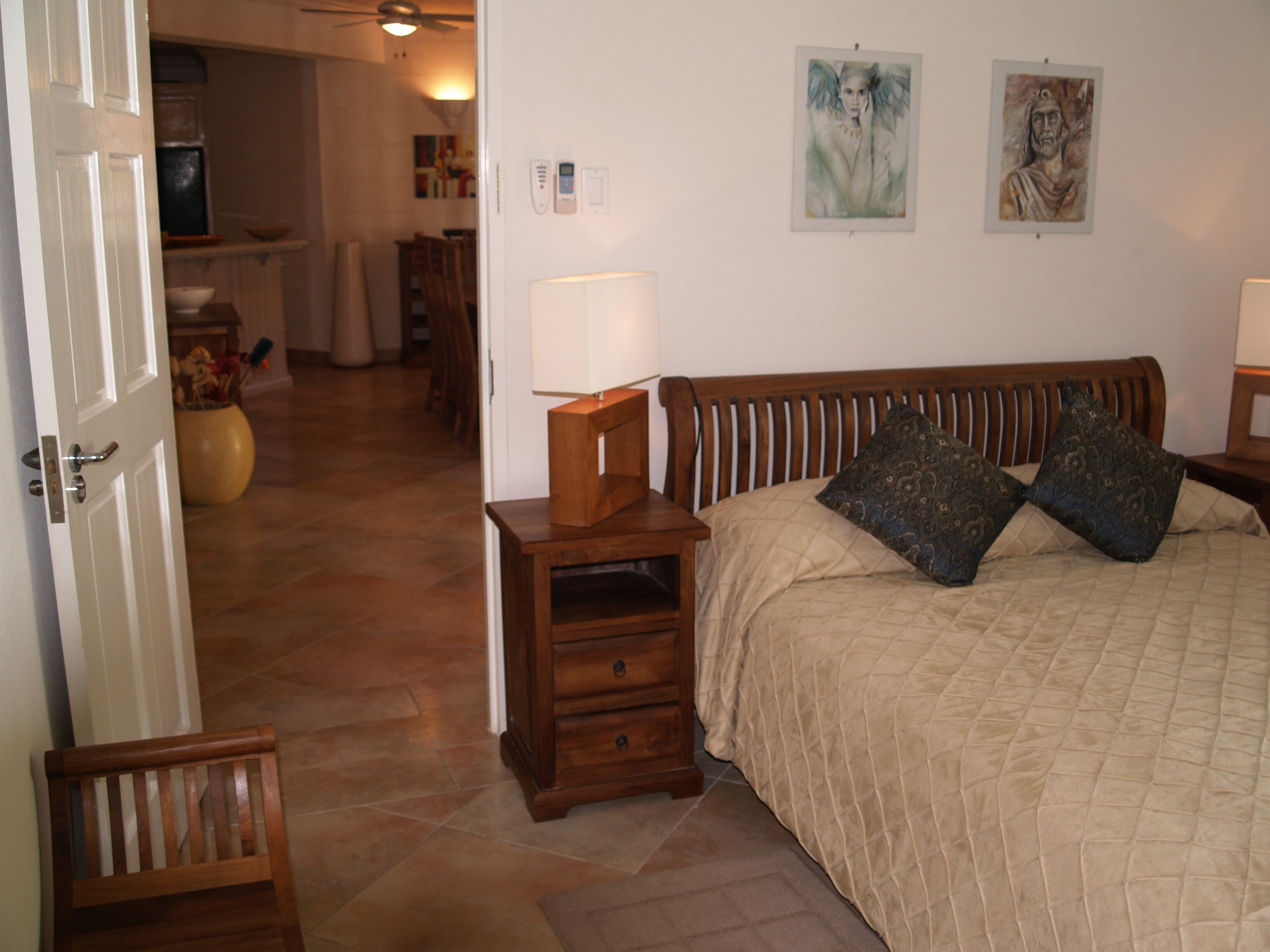 A bedroom with a wooden headboard, a bed with a quilted cover, two bedside lamps, and two wall-mounted paintings.
