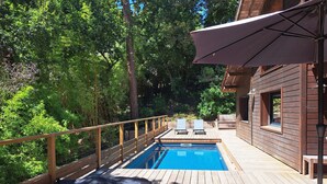 Une terrasse en bois avec une piscine, des chaises longues et un chalet en bois.