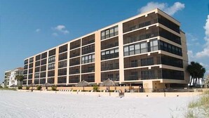 Ein mehrstöckiges Hotel mit schlichter Fassade, großen Fenstern und einem Sandstrand im Vordergrund.