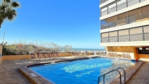 Ein Pool mit freiem Blick auf den Ozean, umgeben von Liegestühlen und einem Gebäude mit Balkonen.