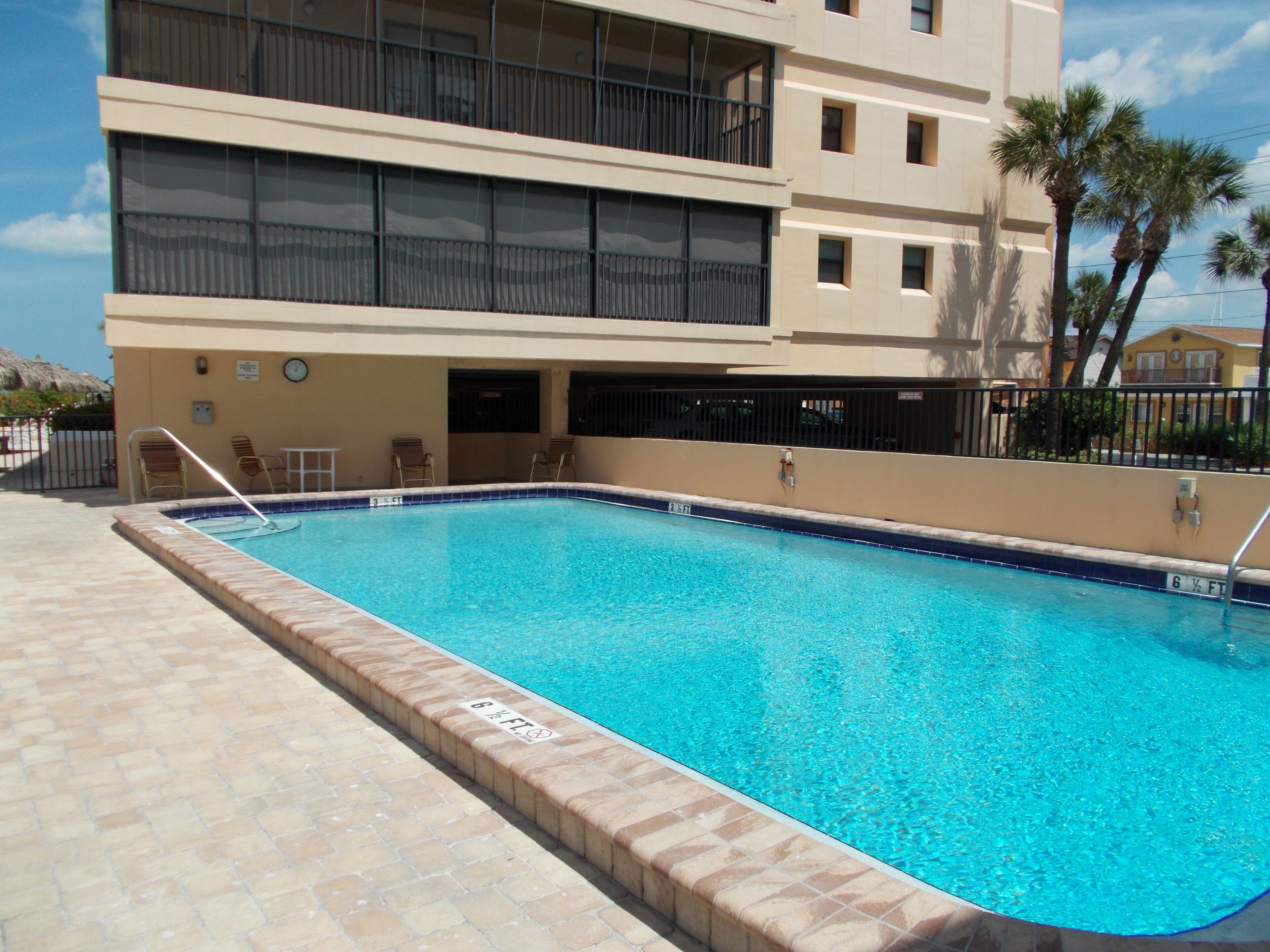 A rectangular swimming pool with a tiled edge, adjacent to a multi-story building with balconies.