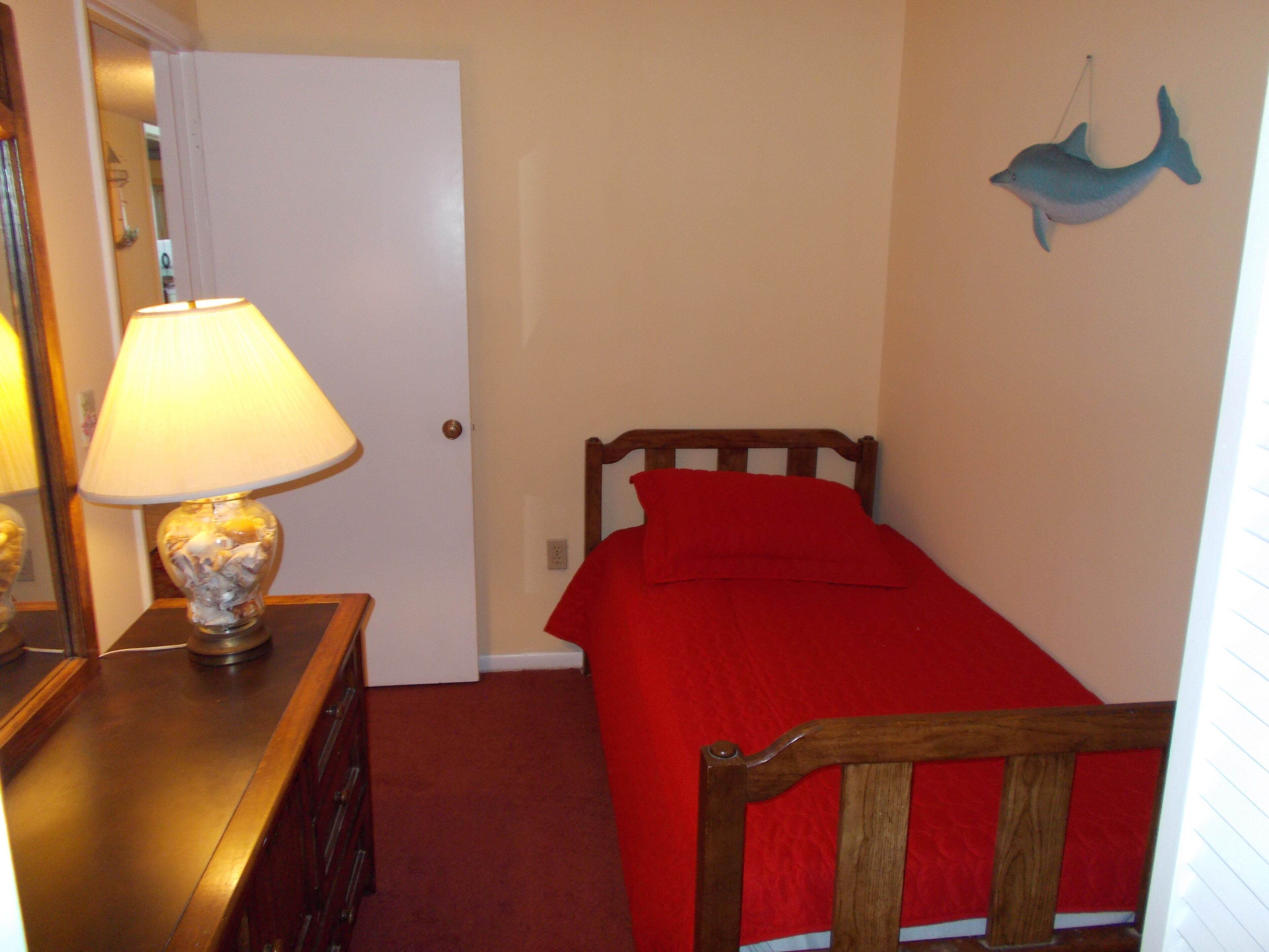 Un dormitorio con una cama de madera, una colcha roja, una lámpara sobre una cómoda de madera y una decoración de delfín en la pared.