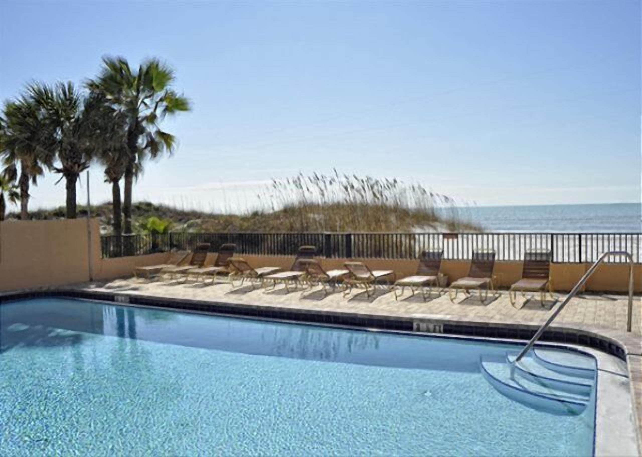 A pool area with lounge chairs and a view of the beach.