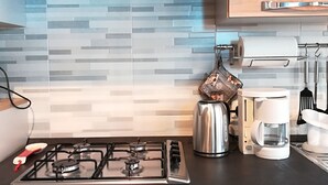 Una cocina con estufa a gas, hervidor, cafetera y salpicadero de azulejos.