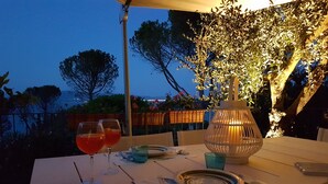 An outdoor dining table set with two glasses of red beverage, a plate, cutlery, and a candle holder.