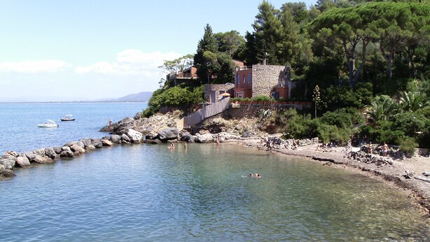 A coastal area with clear water, rocky shore, and a building with stone walls.