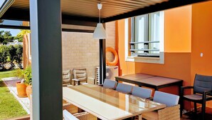 Eine Terrasse im Freien mit einem langen Esstisch, Korbstühlen und einem Deckenventilator.