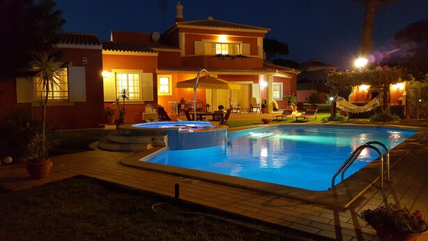 Ein Swimmingpool mit Whirlpool, umgeben von einer Terrasse mit Gartenmöbeln und einem Haus im Hintergrund.