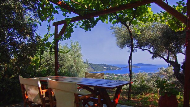 Un espace extérieur aménagé avec une table et des chaises, entouré de verdure et offrant une vue panoramique sur la mer.