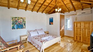 Une chambre avec un plafond en bois, un lit recouvert d’une literie à motifs floraux, une armoire en bois et un téléviseur.