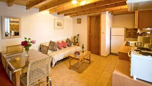 Un salon confortable avec un canapé, une table basse et une table à manger. On peut apercevoir une cuisine équipée d’une cuisinière et d’un réfrigérateur.