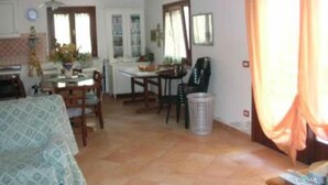 A dining area with a table and chairs, a trash bin, and a window with curtains. - House / Villa - STINTINO (Stintino)