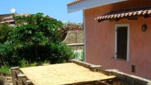 A stone pathway leading to a building with a tiled roof and a wooden structure. - House / Villa - STINTINO (Stintino)