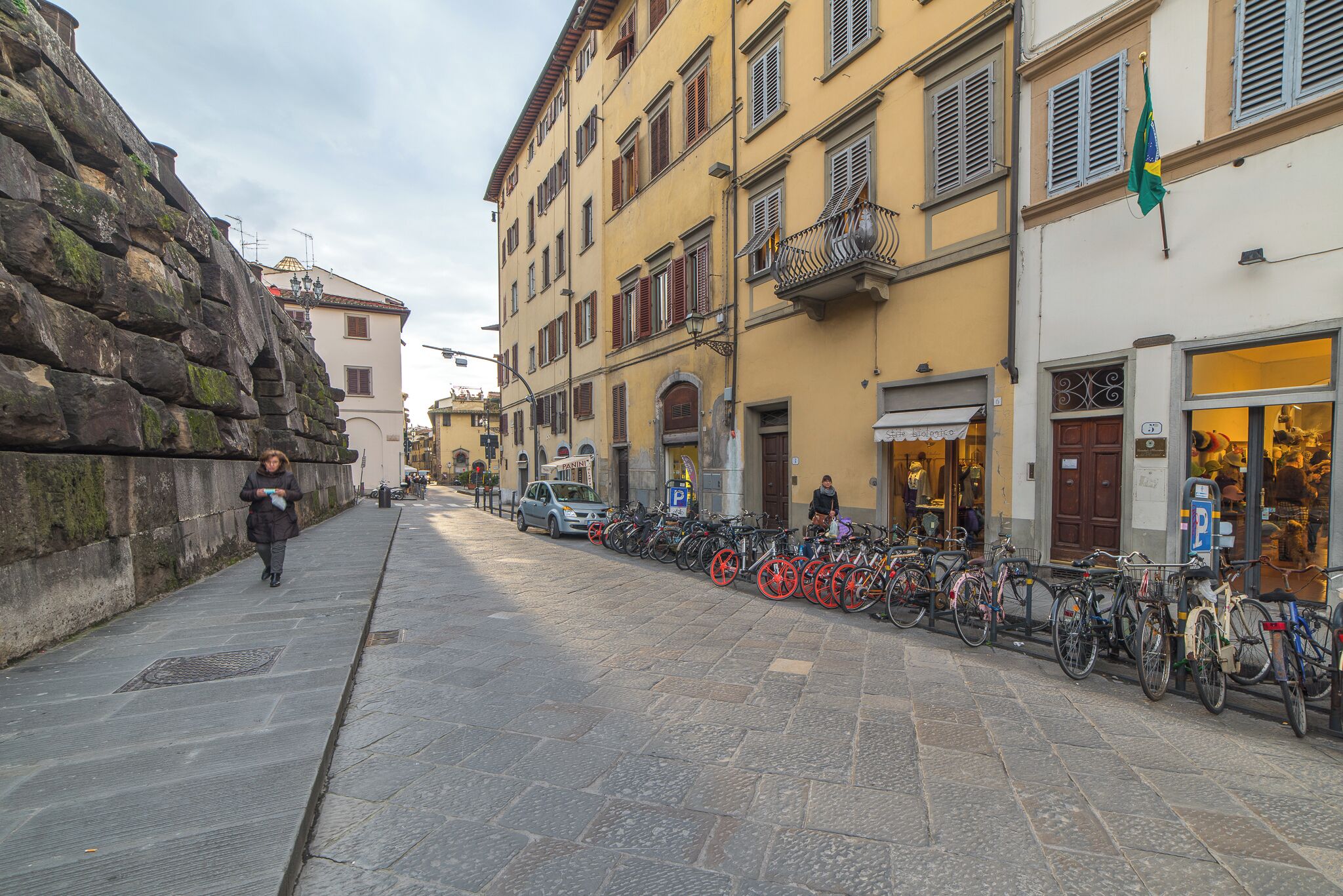 A stone-paved street lined with parked bicycles and a pedestrian walking.