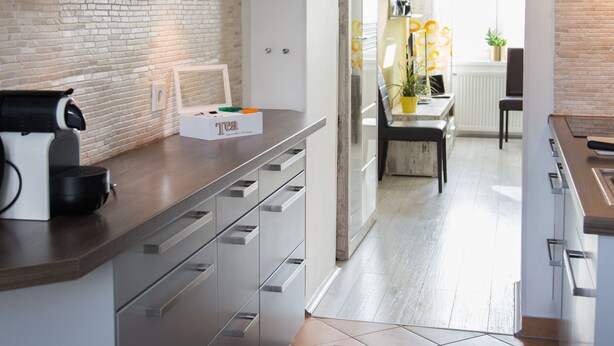 Una cocina moderna con cafetera, una caja de té y un comedor con mesa y sillas.