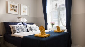 Una cama bien hecha con una colcha azul oscuro y dos toallas dobladas encima. Encima de la cama, hay dos cuadros en la pared.