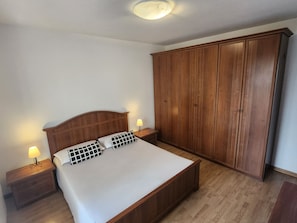 A bedroom with a wooden bed, two bedside tables with lamps, and a large wooden wardrobe.