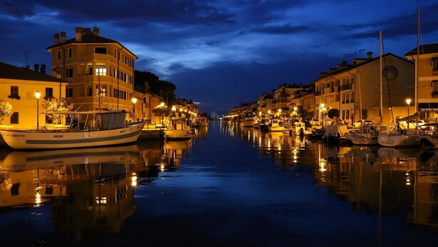 A canal lined with buildings and boats, reflecting the lights on the water.