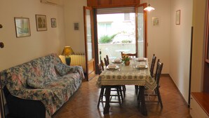 A dining area with a table set for four, a floral sofa, and a window with a view of greenery.