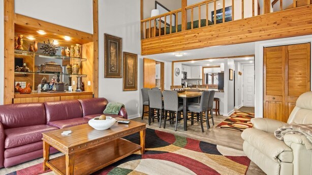 Un vaste espace de vie comprenant un canapé en cuir, une table basse en bois et une table à manger avec des chaises. Un escalier en bois relie les deux niveaux.