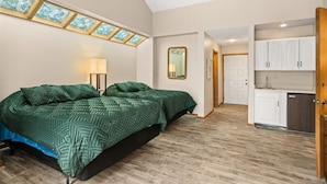 Une chambre avec un grand lit, une lucarne, une table de chevet avec une lampe et une vue sur un coin cuisine.