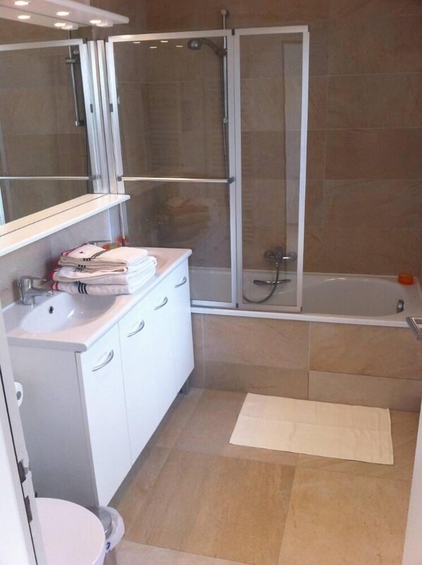 Een moderne badkamer met een douchecabine, een wit badkamermeubel met een wastafel en een bad.
