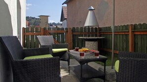 Eine Terrasse im Freien mit Korbmöbeln, einem Tisch mit Getränken und einem Grill.