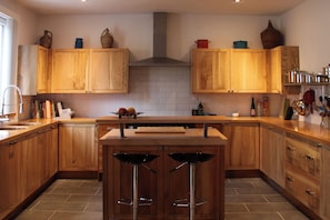 A kitchen with wooden cabinets, a central island with stools, and various kitchen utensils and appliances.