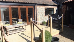A patio with outdoor seating, a stone wall, and a wooden fence. - Recently refurbished barn, close to coast, pet friendly with a secure garden. (Lessingham)