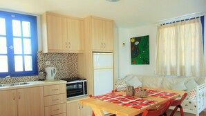 A compact kitchen with wooden cabinets, a microwave, and a refrigerator. There's a dining table with a colorful rug and a sofa with cushions. - Sunny with sea view apartment (Santorini)
