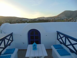 A white building with a blue door and windows, a white table with a blue birdhouse, and blue cushions on white benches. - Sunny with sea view apartment (Santorini)