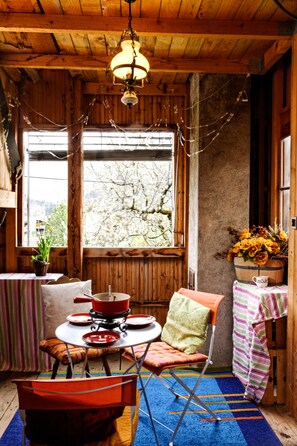 Interior acogedor de una cabaña con techo de madera, una mesa de comedor con sillas, un ventanal con vistas a árboles y una mesita con planta en maceta.