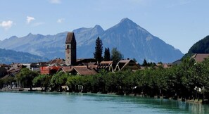A lakeside town with a prominent church tower, surrounded by traditional buildings and mountains in the background.